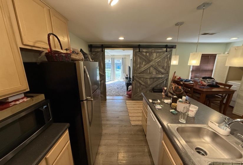 Kitchen with dark countertops, a barn door, stainless steel microwave, dark wood-style flooring, and decorative light fixtures