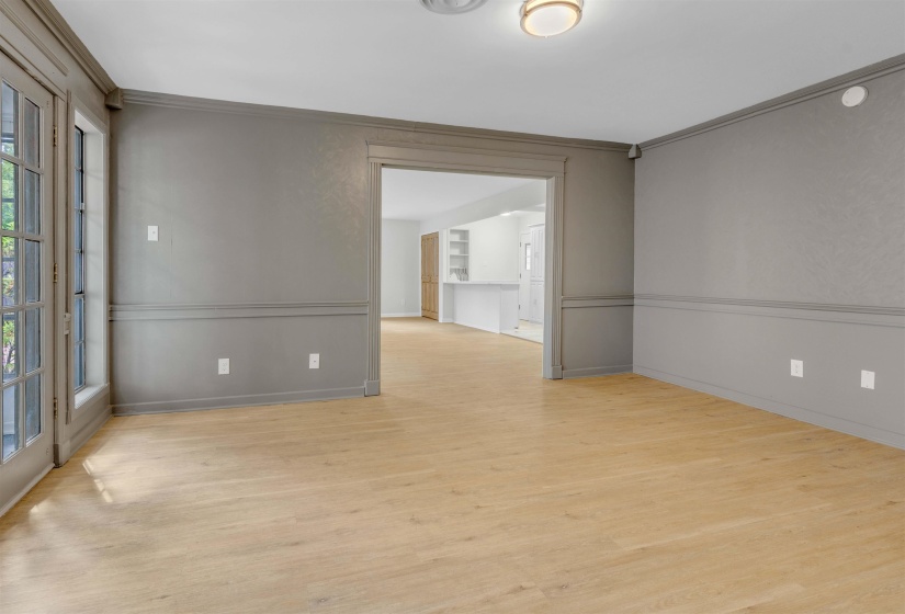 Spacious room featuring wood-finish flooring, neutral gray walls with chair rail molding, and a wide cased opening