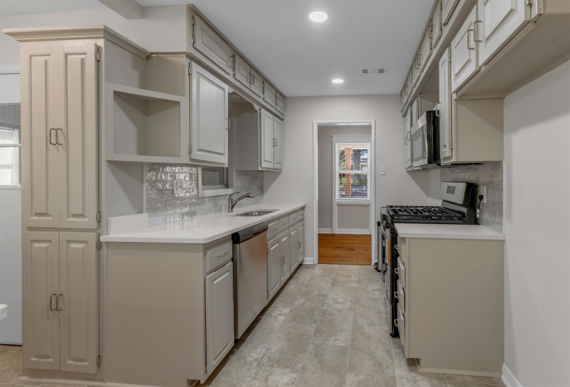 Galley kitchen featuring light-toned cabinetry, stainless steel appliances, white countertops, a tiled backsplash, and recessed lighting
