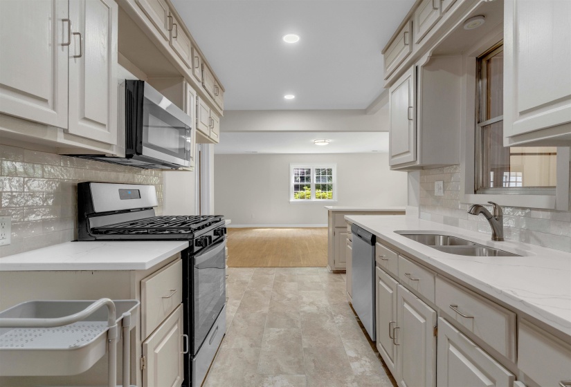 Galley kitchen featuring light-toned cabinetry and countertops, a stainless steel gas range, over-the-range microwave, and a double basin sink