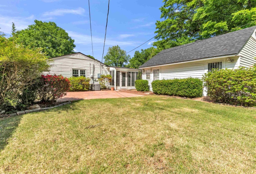 Expansive backyard featuring a large green lawn, mature landscaping with flowering shrubs, and a spacious concrete patio