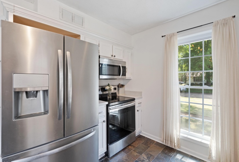 Stainless steel French door refrigerator with an external ice and water dispenser, complemented by a stainless steel range and microwave
