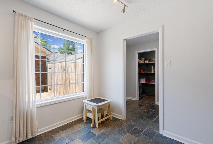 Spacious room featuring a large gridded window, slate tile flooring, track lighting, and a pantry with built-in shelving