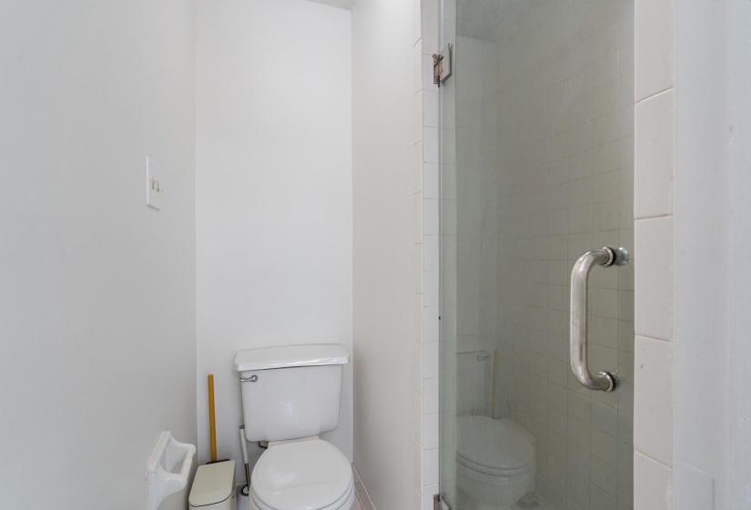 White toilet with a glass-enclosed shower featuring a tiled interior and a chrome handle