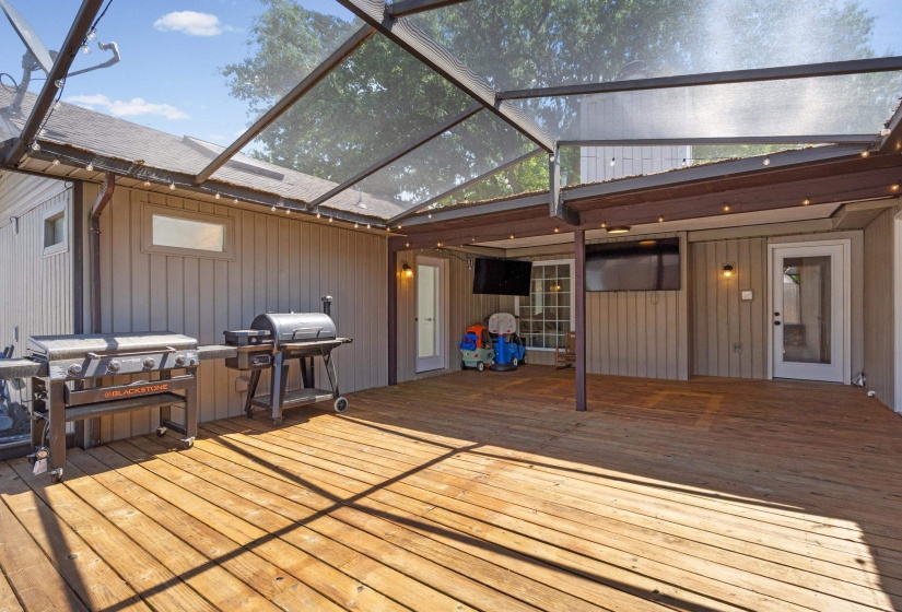 Expansive wood-finish deck under a screened enclosure with built-in string lighting, offering an extended outdoor living area
