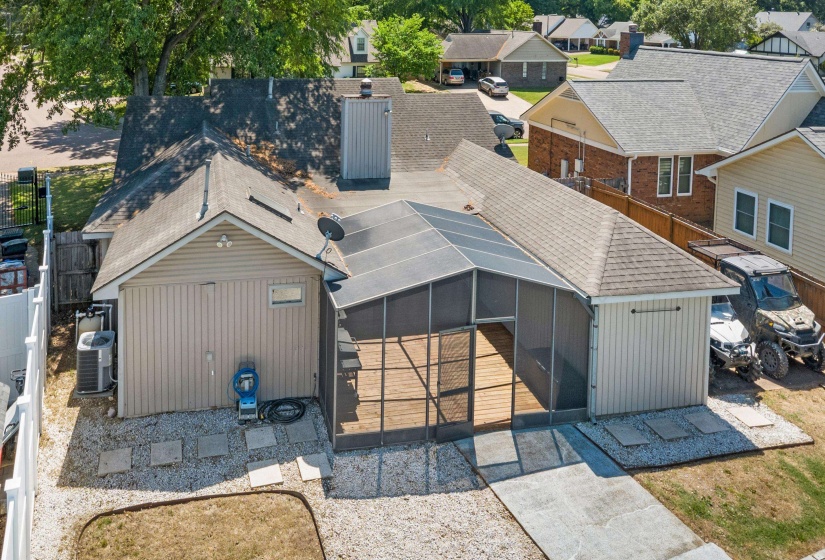 Rear exterior featuring a screened-in patio with wood-finish flooring, a detached storage building with vertical siding, and a gravel yard with stepping stones