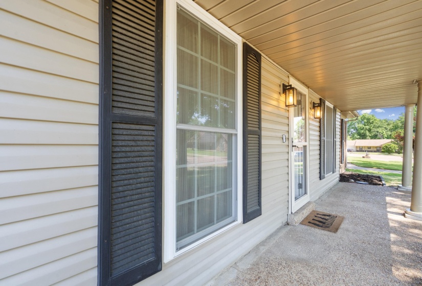 Front porch featuring light-toned siding, black louvered shutters, and dual exterior wall sconces