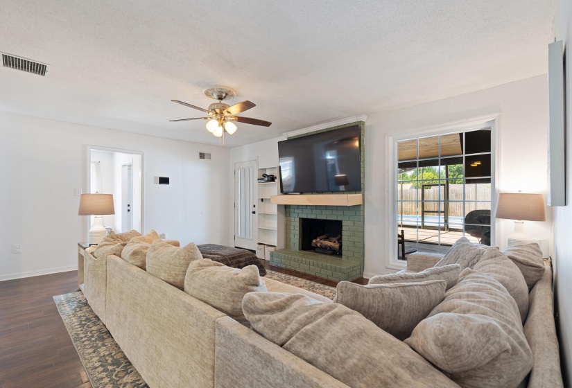 Spacious living area featuring wood-finish flooring, a ceiling fan, and a fireplace with green tile surround and built-in shelving