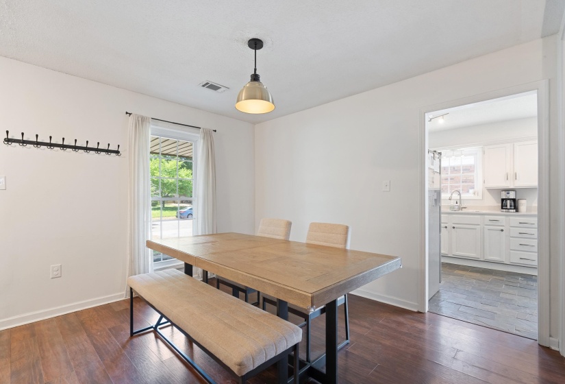Dining area featuring wood-finish flooring, a contemporary pendant light fixture, and a window with white curtains
