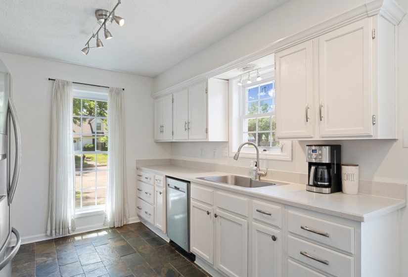 Kitchen featuring white cabinetry with brushed nickel hardware, light-toned countertops, a stainless-steel sink with a gooseneck faucet, and dark slate-style floor tiling