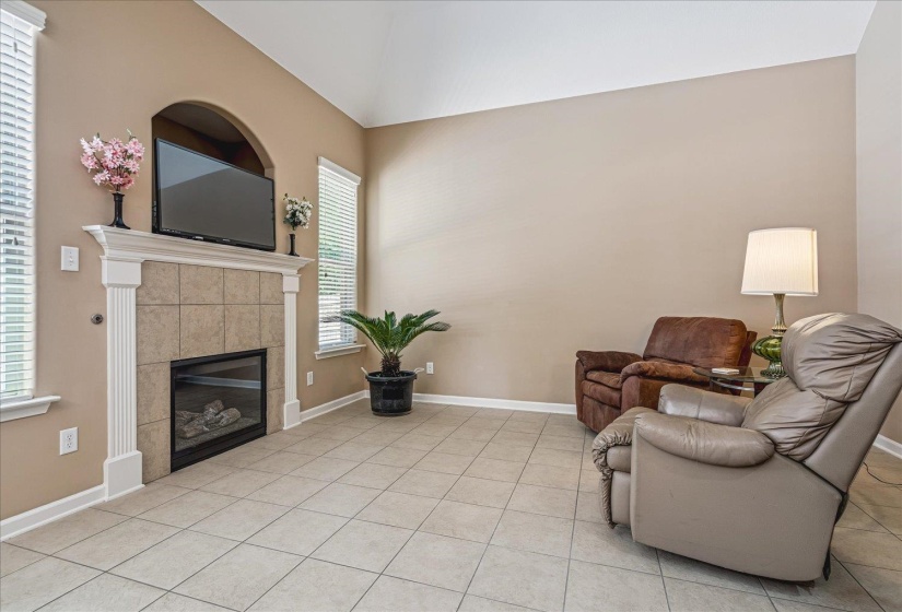 Hearth Room featuring a tile-surround gas fireplace with a white mantel, vaulted ceilings, and tile flooring.