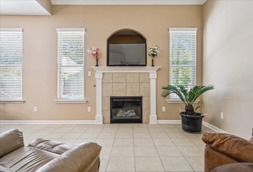 Hearth Room featuring a tile-surround gas fireplace with a white mantel, vaulted ceilings, and tile flooring.