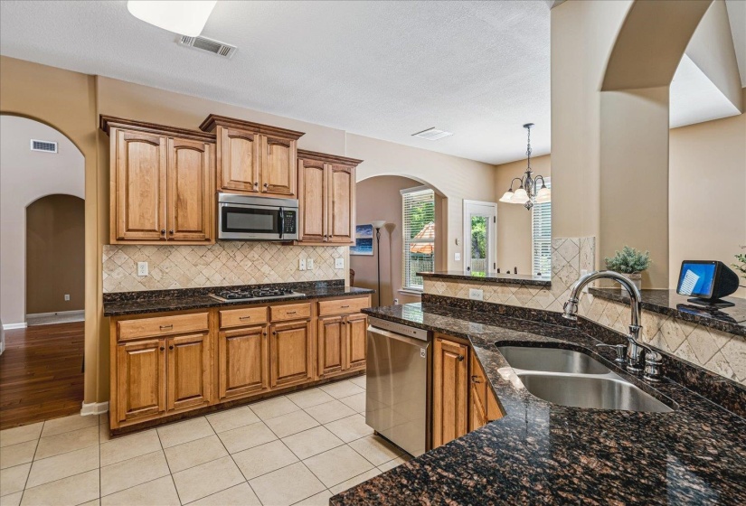 Kitchen featuring granite countertops, wood cabinetry, stainless steel appliances, tile flooring, and a decorative tile backsplash.