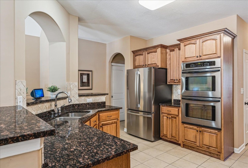 Kitchen featuring granite countertops, wood cabinetry, stainless steel appliances, and tile flooring