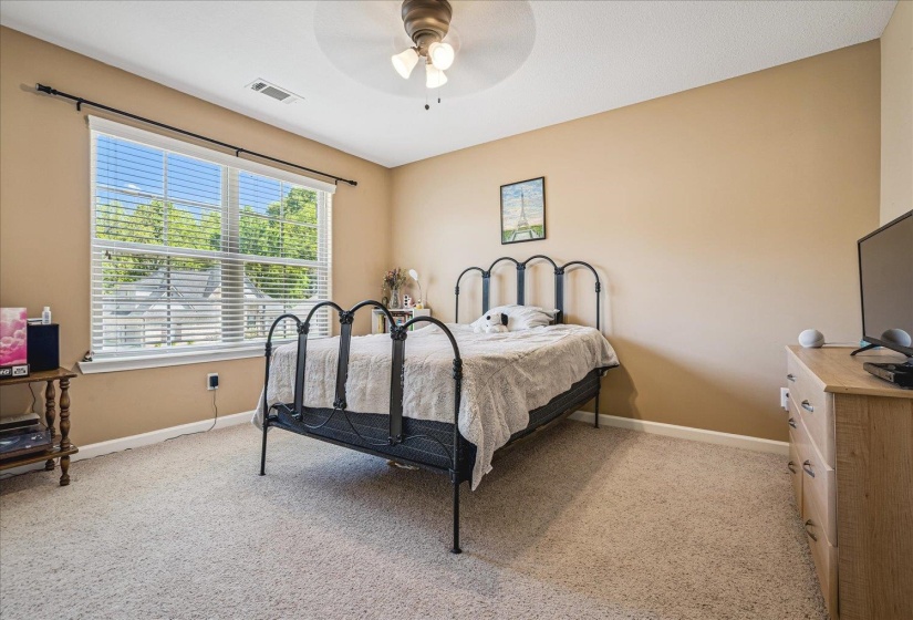 Carpeted bedroom featuring a large window with blinds, a ceiling fan, and neutral-toned walls.Located on second story.