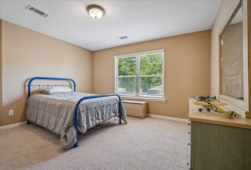 Carpeted bedroom featuring a large window with blinds, a ceiling fan, and neutral-toned walls.Located on second story.