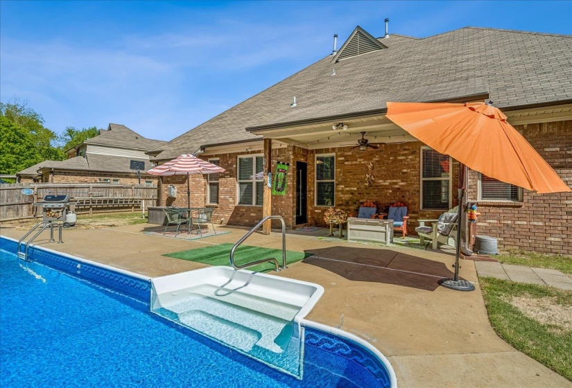 Expansive backyard featuring a rectangular in-ground swimming pool with integrated steps, a surrounding concrete patio, and a covered back patio. Salt Water System.New liner. Covered Patio.