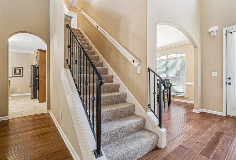 Foyer featuring wood flooring, a carpeted staircase with wrought iron balusters, and arched doorways