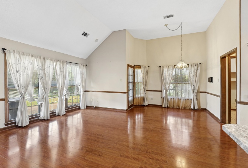 Expansive living area featuring warm wood-finish flooring, a vaulted ceiling, and multiple windows