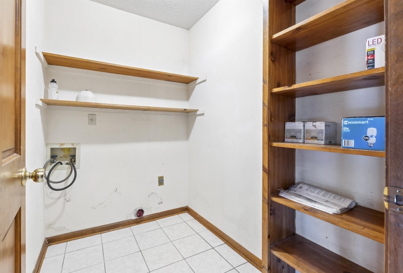 Utility space featuring a wood-finish door, white square tile flooring, wood-finish baseboards, and two floating wood-finish shelves
