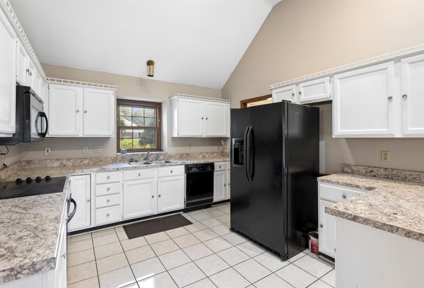 Kitchen featuring white cabinetry, light-toned countertops, a full suite of black appliances, tile flooring, and a vaulted ceiling