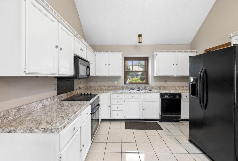 Kitchen featuring white cabinetry, light-toned countertops, a black refrigerator, a built-in microwave, and tile flooring