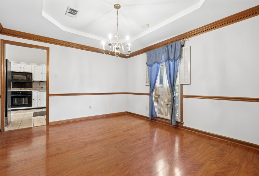 Spacious room featuring wood-finish flooring, white walls with brown chair rail molding, and a tray ceiling with a brass chandelier