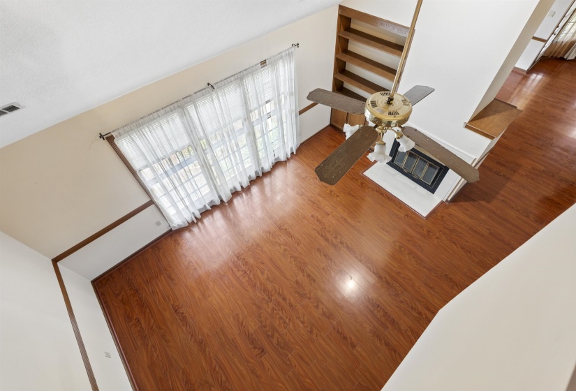Spacious living area featuring wood-finish flooring, a ceiling fan with light fixture, and a white fireplace hearth