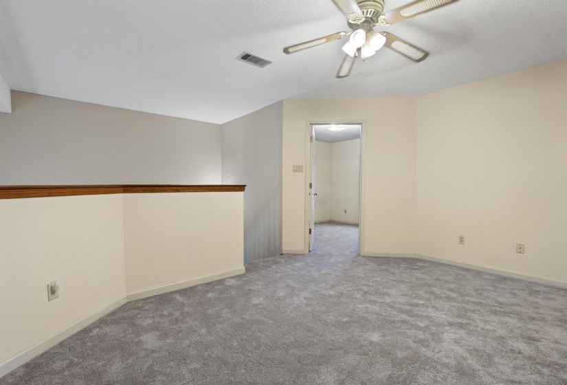 Carpeted room featuring a ceiling fan with integrated lighting, a half-wall with wood-finish railing, and neutral wall tones