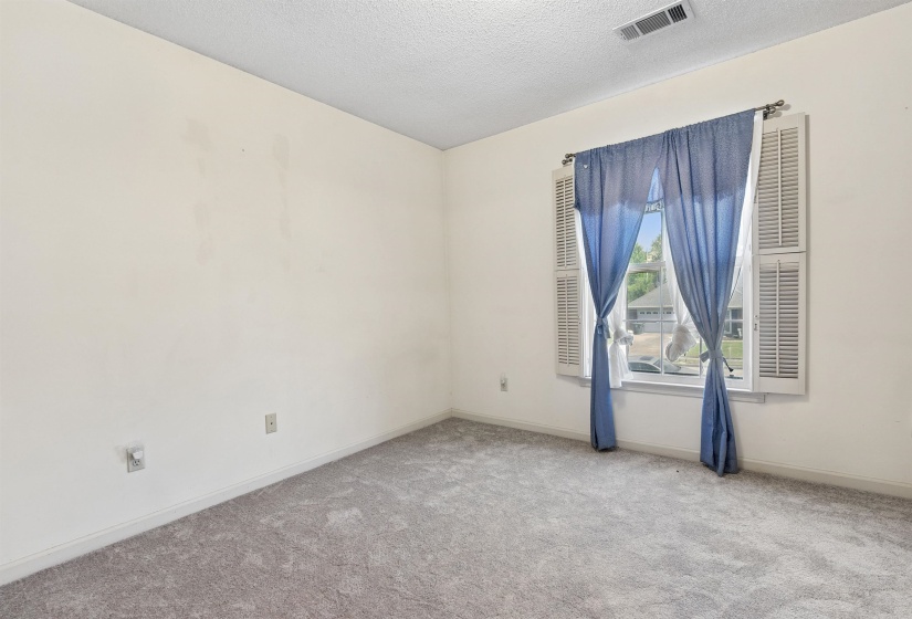 Carpeted interior room featuring a window with white louvered shutters, a white ceiling with a single ventilation register, and baseboard trim