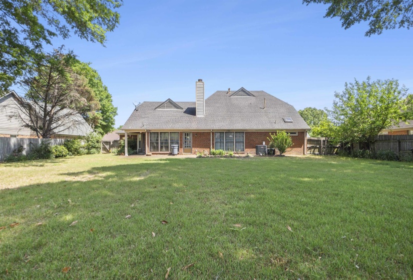 Expansive rear lawn featuring a brick exterior, covered patio, multiple windows, and a multi-dimensional shingled roof with dormer accents