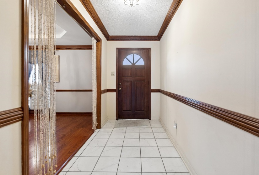 Entryway featuring a wood-paneled door with an arched window, white tile flooring, and decorative wood trim
