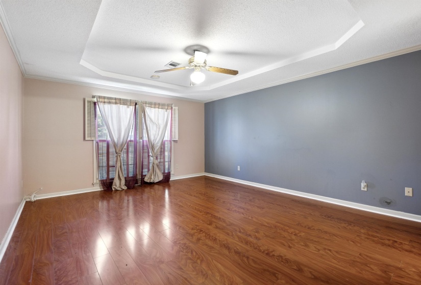 Spacious room featuring wood-finish flooring and a tray ceiling with a ceiling fan