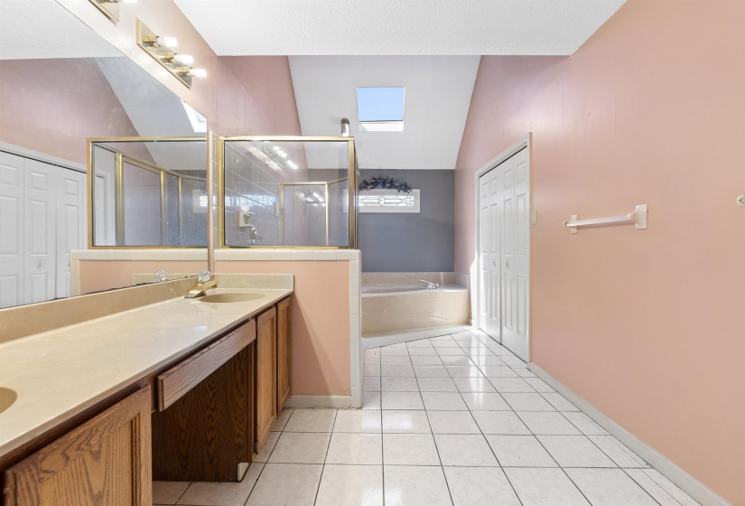 Spacious bathroom featuring a dual vanity with light-colored countertops, a glass-enclosed shower, and a built-in corner bathtub
