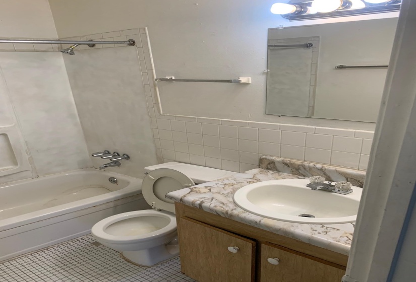 Full bathroom with tile walls, bathing tub / shower combination, vanity, tile patterned flooring, and a wainscoted wall