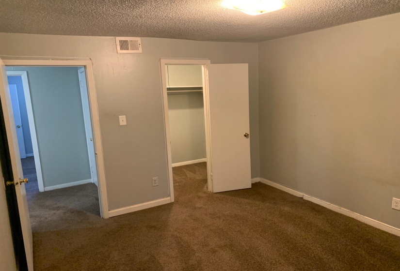 Unfurnished bedroom with dark carpet, a textured ceiling, and a spacious closet