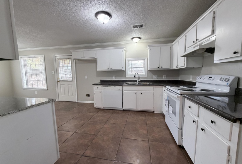 Kitchen with white appliances, ornamental molding, white cabinetry, under cabinet range hood, and a textured ceiling
