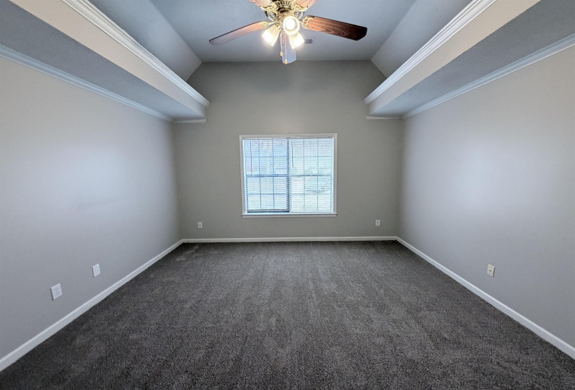 Spare room featuring crown molding, vaulted ceiling, dark colored carpet, and ceiling fan