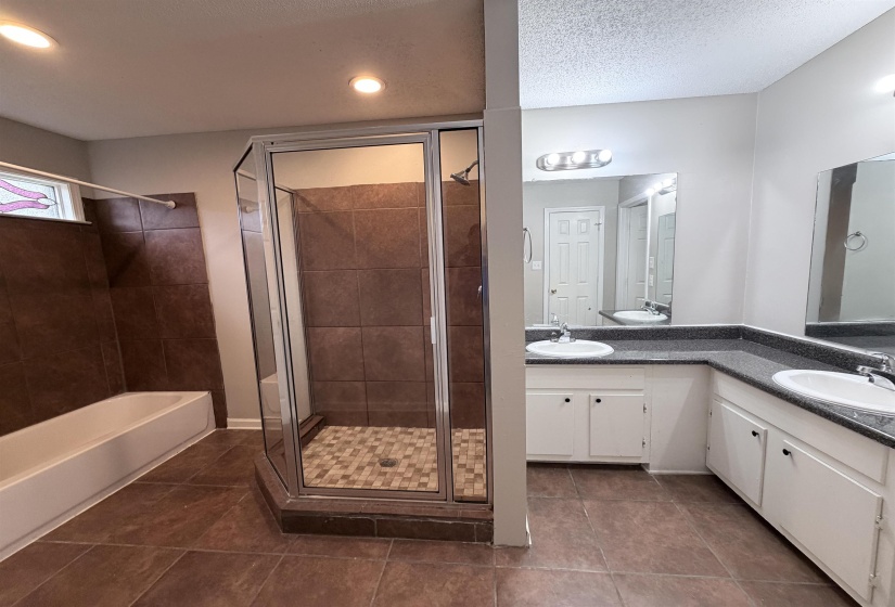 Bathroom with dark tile patterned flooring, a stall shower, double vanity, a textured ceiling, and a tub to relax in