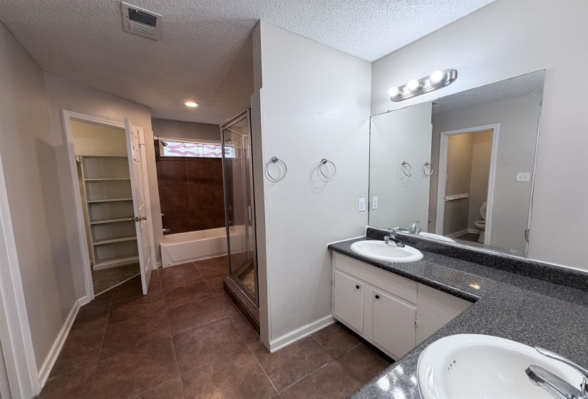 Bathroom featuring double vanity, a tub, a stall shower, dark tile patterned flooring, and a textured ceiling