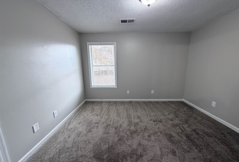Carpeted empty room with a textured ceiling and baseboards