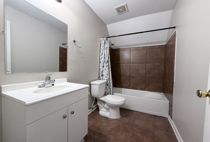 Full bathroom featuring vanity, shower / bath combo, a textured ceiling, and dark tile patterned floors