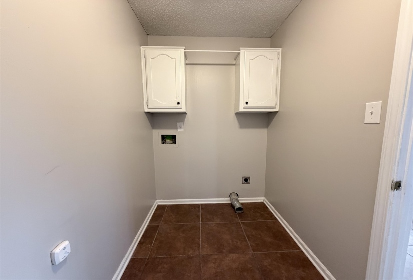 Laundry room featuring cabinet space, a textured ceiling, hookup for a washing machine, electric dryer hookup, and dark tile patterned floors