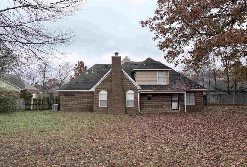 Back of house featuring a fenced backyard, a chimney, brick siding, and roof with shingles