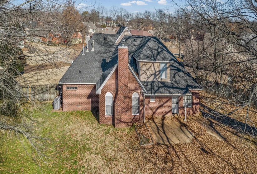 View of side of property featuring a chimney, brick siding, roof with shingles, and a yard