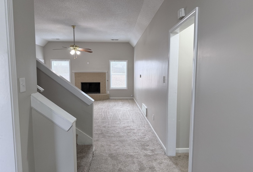 Hallway with light colored carpet, vaulted ceiling, and a textured ceiling