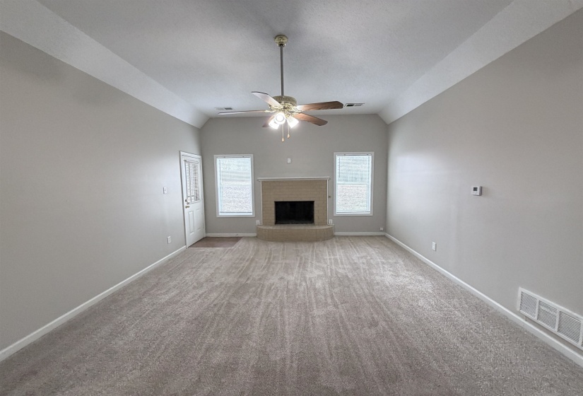 Unfurnished living room featuring lofted ceiling, a fireplace, carpet floors, and a ceiling fan