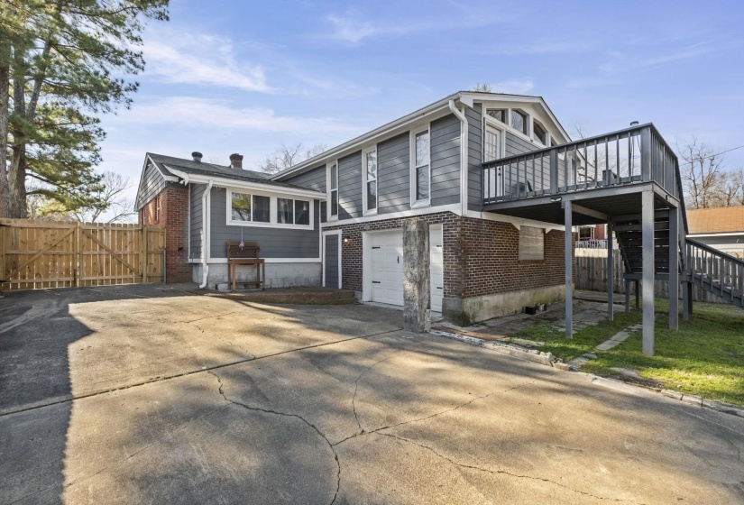 Rear view of house with brick siding, a garage, concrete driveway, a deck, and stairway