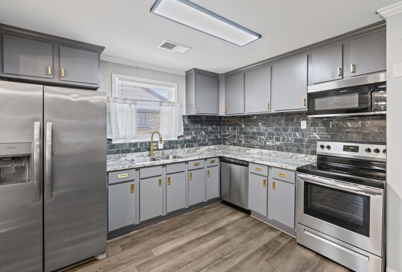 Kitchen featuring gray cabinets, stainless steel appliances, ornamental molding, tasteful backsplash, and light wood finished floors