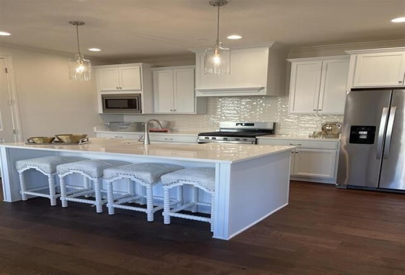Kitchen featuring a central island with countertop seating, white shaker-style cabinetry, stainless steel appliances, and wood-finish flooring